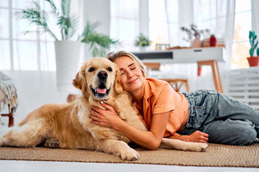 7 Expert Tips for Keeping Your Dog Out of Trouble When You're at Work 5 A woman lies on the floor hugging her happy golden retriever in a bright living room. Bonding and affection are essential tips for keeping your dog out of trouble through emotional security.