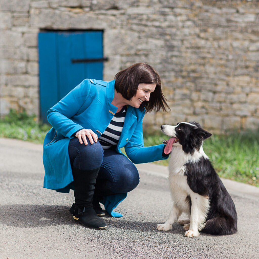 Can Dogs Laugh? And What That Breathy Panting Sound Actually Means 1 A woman in a blue coat kneeling and stroking a black and white collie.