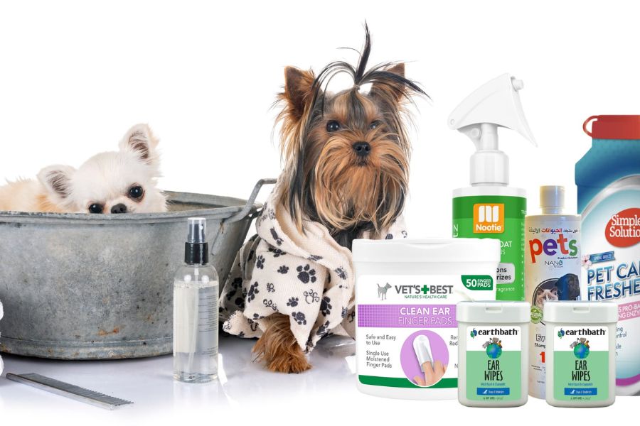 10 Essential Items Every Pet Owner Needs In Their Cupboards When Disaster Strikes 1 Two small dogs, one in a metal tub and the other in a paw-print robe, surrounded by grooming and cleaning products, showcasing essential Items Every Pet Owner Needs for hygiene and care.